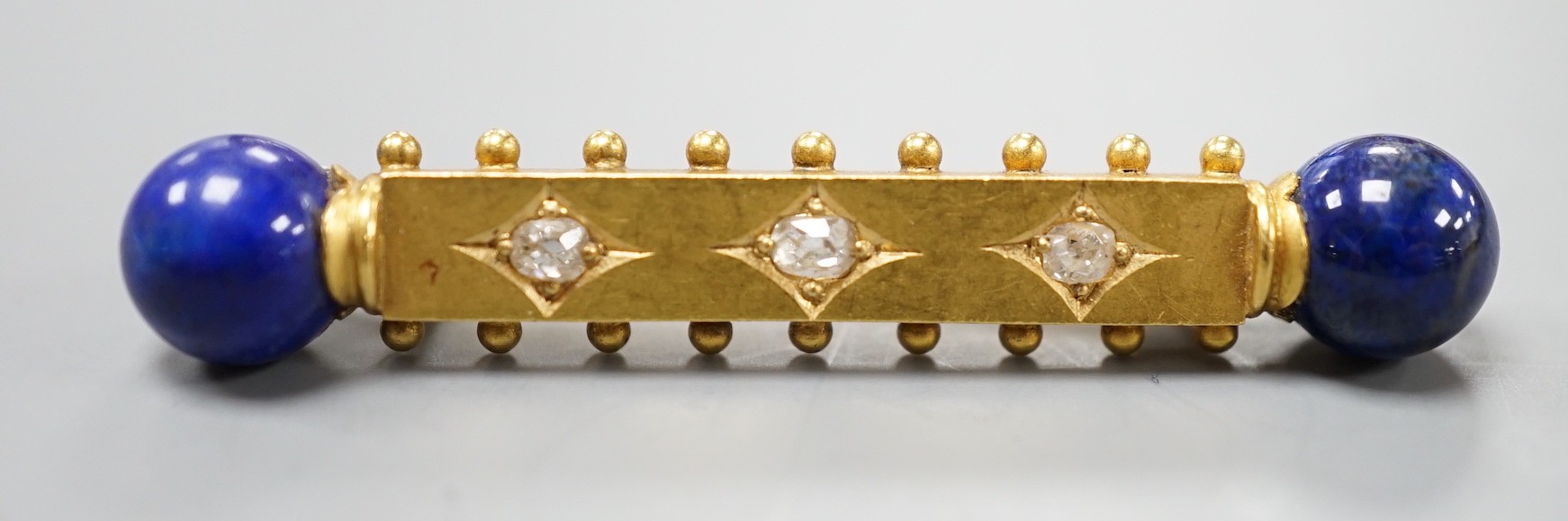 A yellow metal and three stone diamond set bar brooch. with lapis lazuli bead set terminals, 43mm, gross weight 4.8 grams.